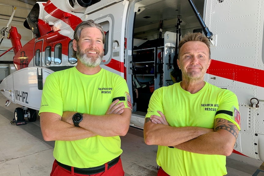 Two men wearing red flight suits sit on a rescue helicopter. 