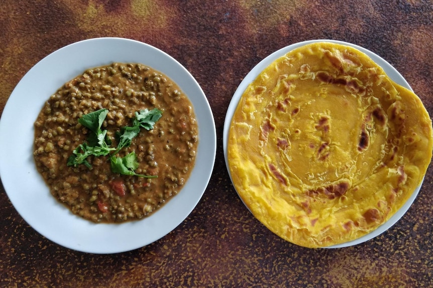 Bird's eye view of a bowl of mung bean cury next to a plate with roti.