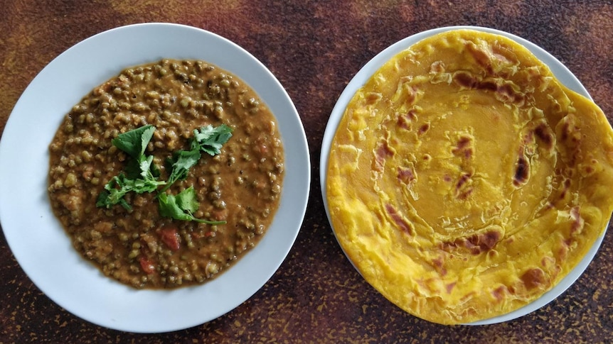 Bird's eye view of a bowl of mung bean cury next to a plate with roti.