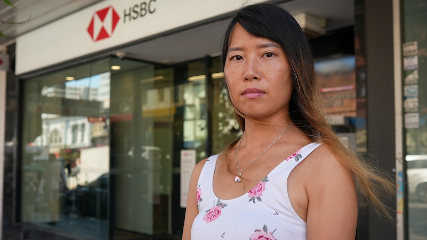 A woman of Asian background with long hair standing out the front of an HSBC bank branch