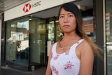 A woman of Asian background with long hair standing out the front of an HSBC bank branch
