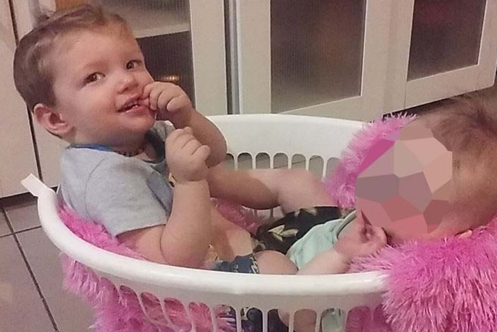Toddler Mason Jet Lee looks up as he sits in a washing basket with another anonymous child.