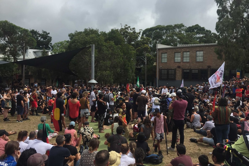 A crowd displaying Indigenous flags gather at the housing development