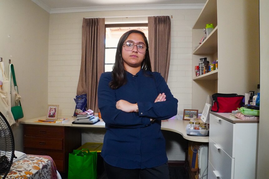 Woman stands with arms crossed in small room