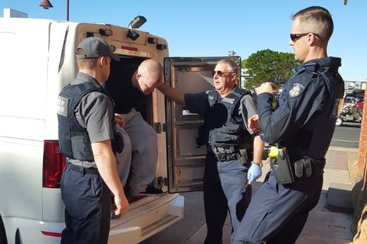 Three policemen lead a man out of a van.