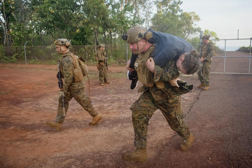 Marines running through dirt, one carrying someone over their shoulder