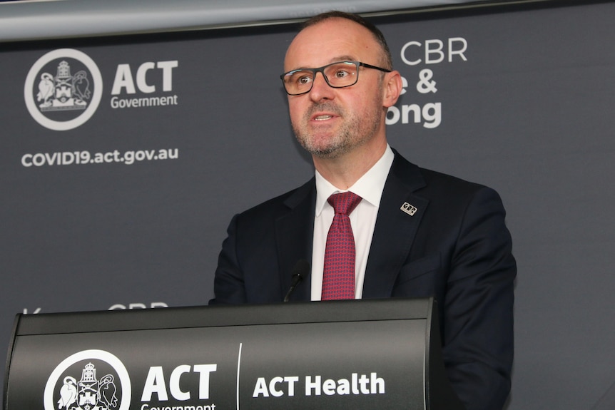 A man wearing a suit stands in front of a lectern 