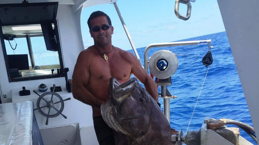 A deep sea fisherman holds up a huge reef fish caught on a line from his boat