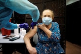a woman in a blue dress and a mask receives a vaccination from a person in PPE