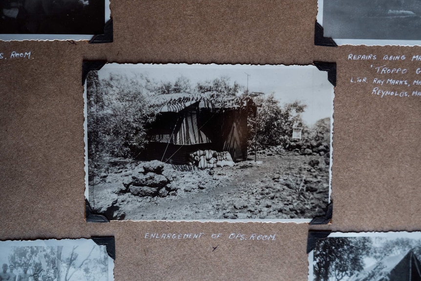 Image of a black and white photo, stuck in an album. The photo details a small military building on a remote island during WWII.