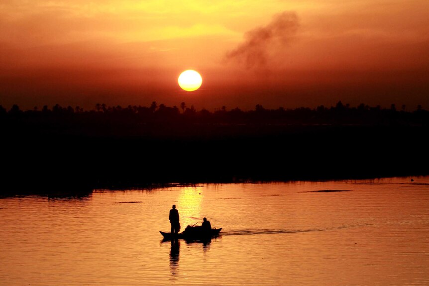 A boat rides along the Euphrates river during golden sunset