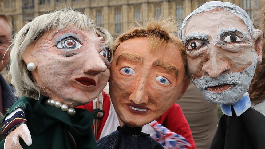 Caricatures of puppet caricatures of theresa may, time farron and jeremy corbyn outside the houses of parliament.