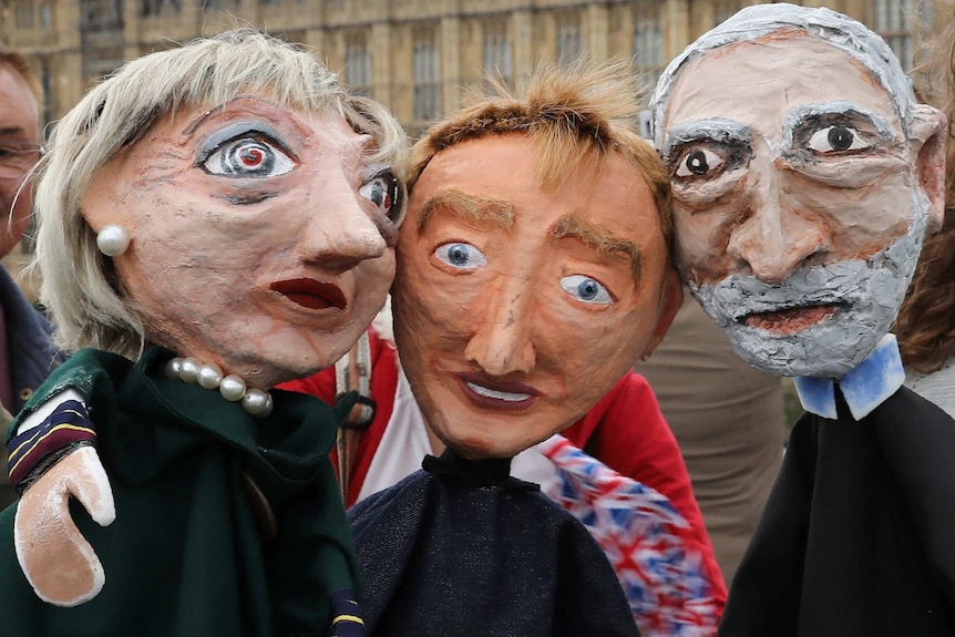 Caricatures of puppet caricatures of theresa may, time farron and jeremy corbyn outside the houses of parliament.