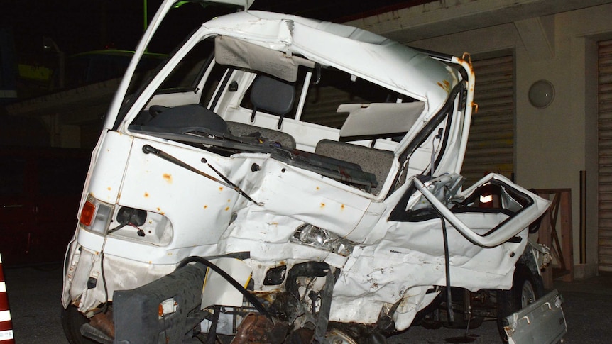 A mangled white van sits on tarmac in front of a building.
