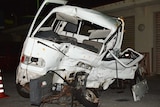A mangled white van sits on tarmac in front of a building.