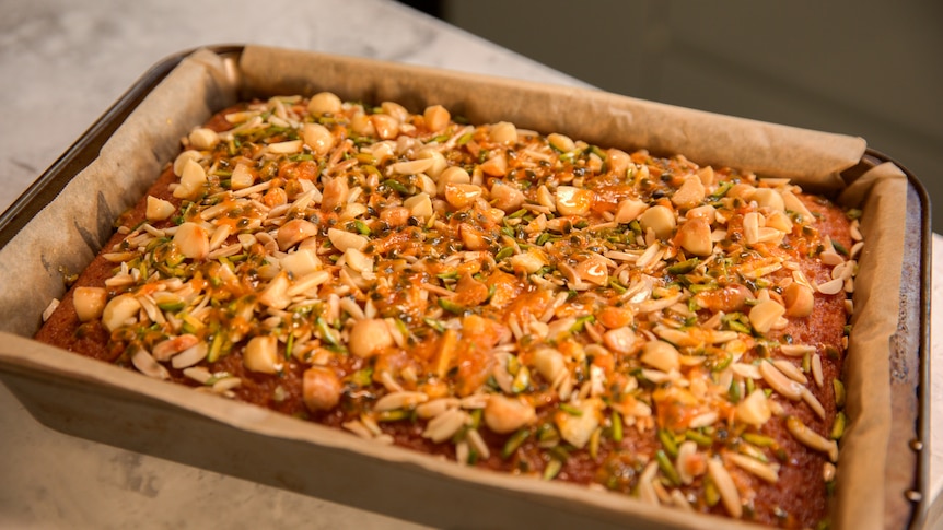 A slice in a baking tin topped with nuts and seeds and glistening with honey.