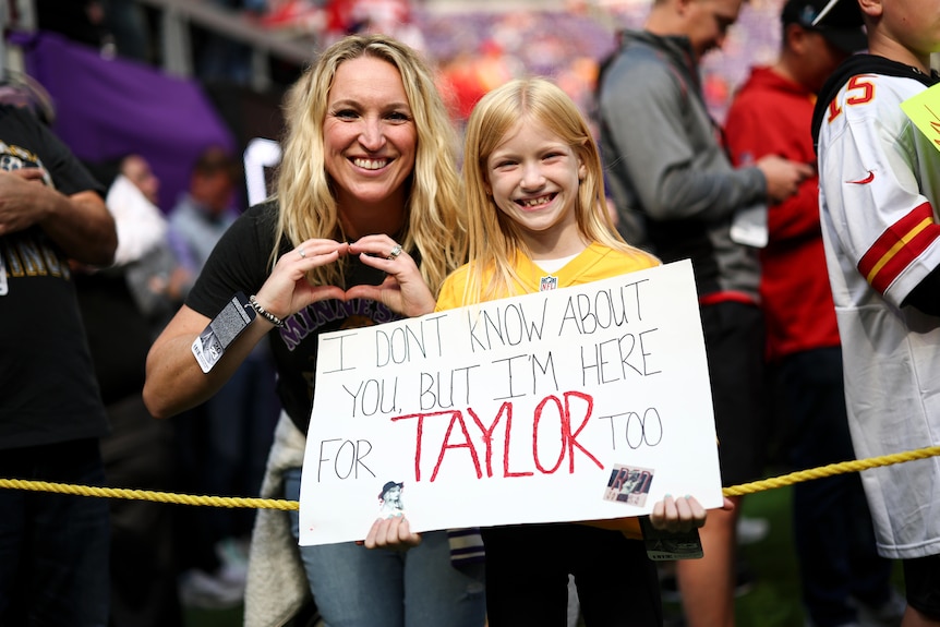 A fan holds a sign saying I don't know about you but I'm here for Taylor too