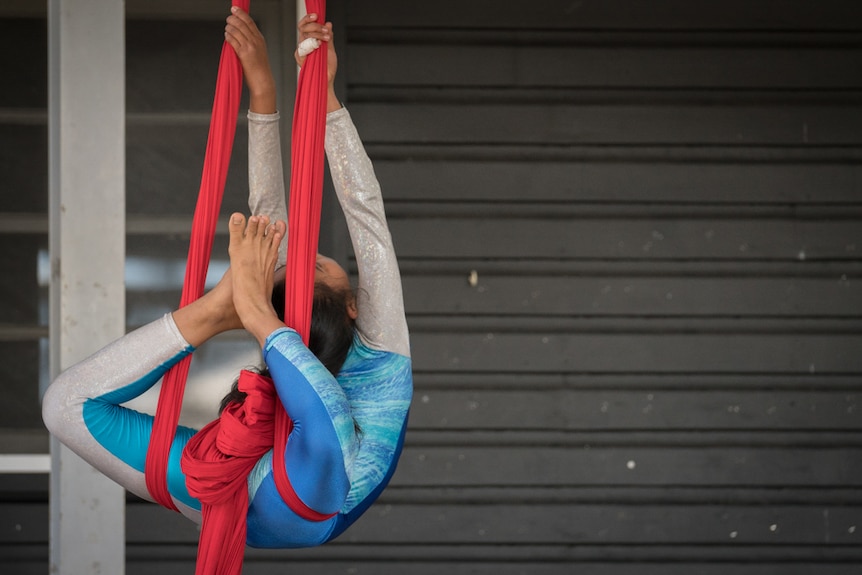 Young girl doing a circus trick on suspended red fabric in a circus act know as acrobatic tissue.