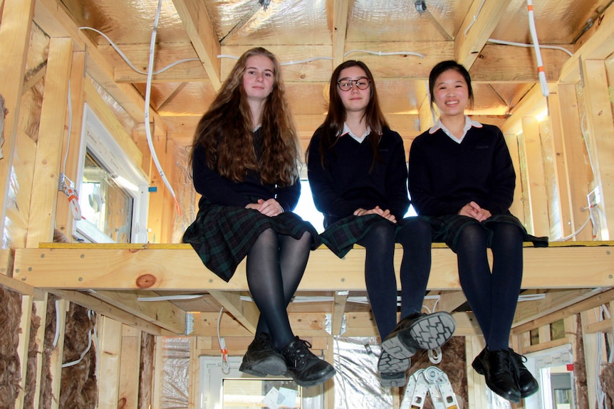 Three students sit inside a tiny house under contstruction