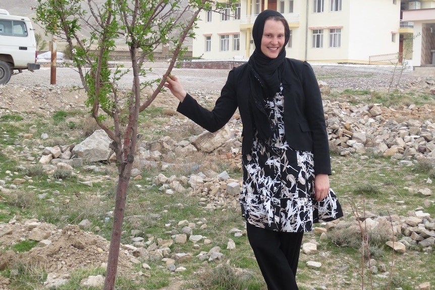 A woman stands next to a tree.