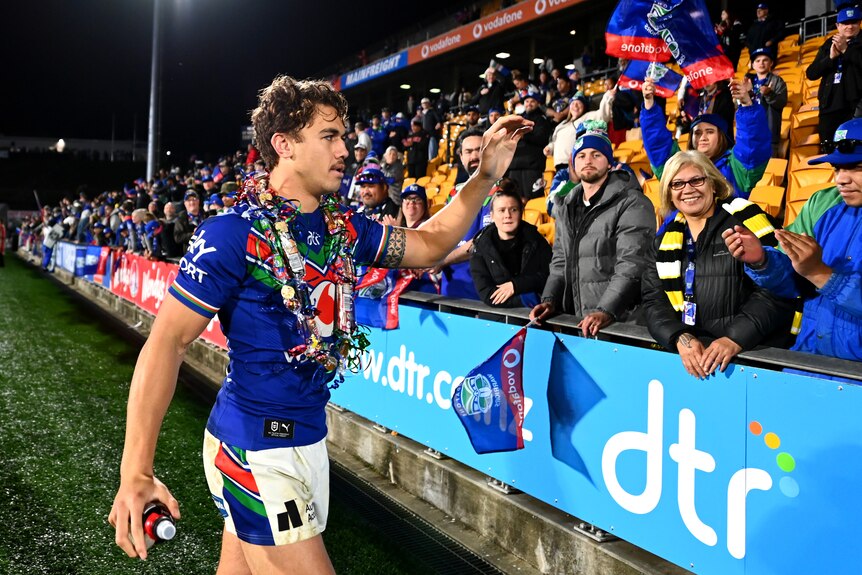 An NRL player raises his hand to acknowledge the fans as he walks off the ground after a victory.