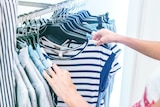 a shopper browsing through a rack of clothes stops to look closely at a t-shirt