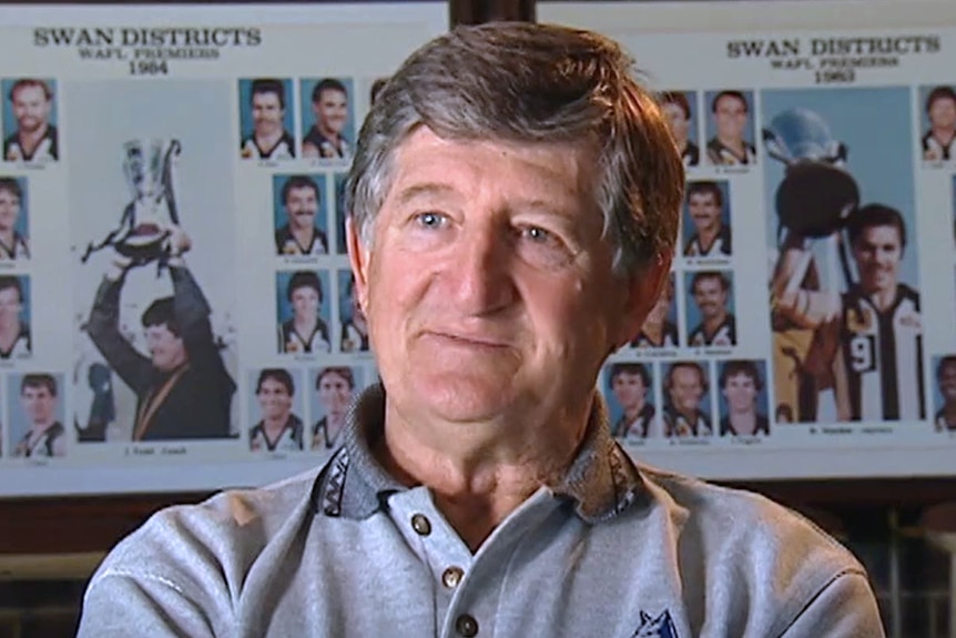 A headshot of John Todd talking during a TV interview, sitting in front of photo frames showing Swan Districts football teams.