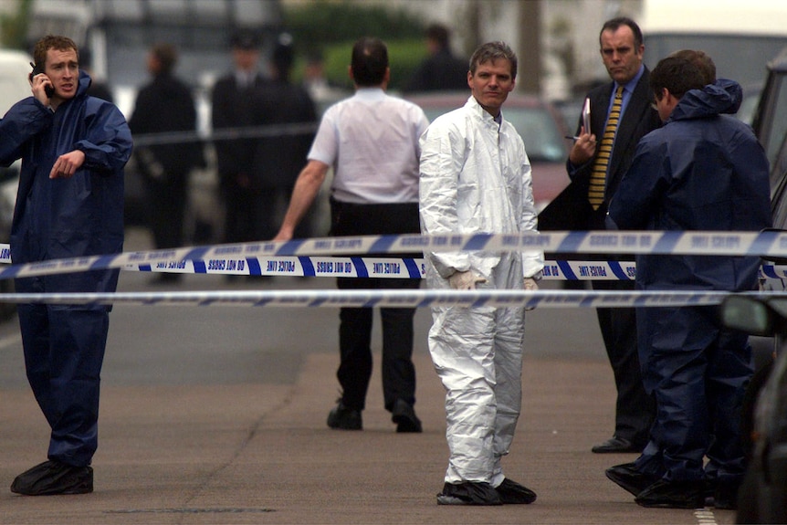 Police stand behind crime scene tape on a street 