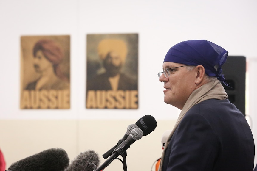 Morrison stands wearing a bandana, with political posters in the background showing Sikh men and labelled 'AUSSIE'.