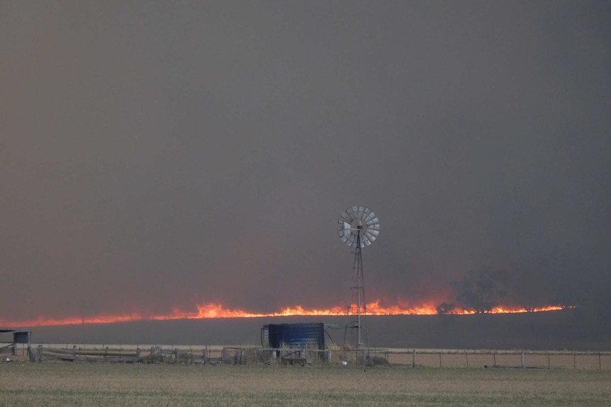 A bushfire burns behind a windmill and water tank near Uarbry.