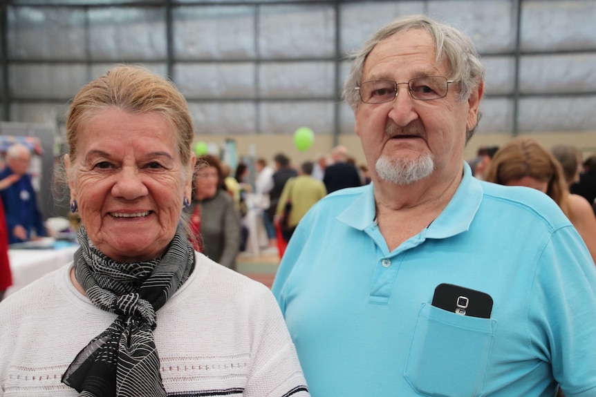 Glenda and Colin Best standing at a convention with lots of people in the background.