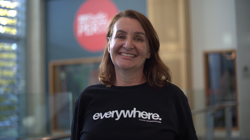 Woman in black t-shirt, brown hair, smiling at camera