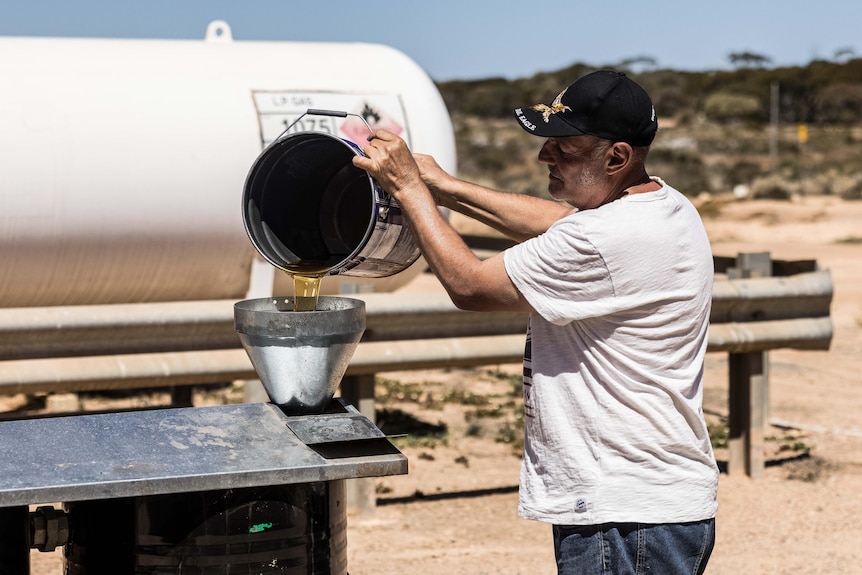 A man pours vegetable oil into a drum.  