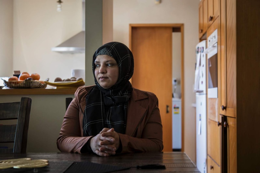 A woman in a headscarf looking pensive while sitting at the kitchen table