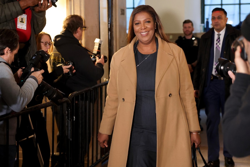 Letitia James smiles as she walks through the courthouse past photographers standing behind a fence.