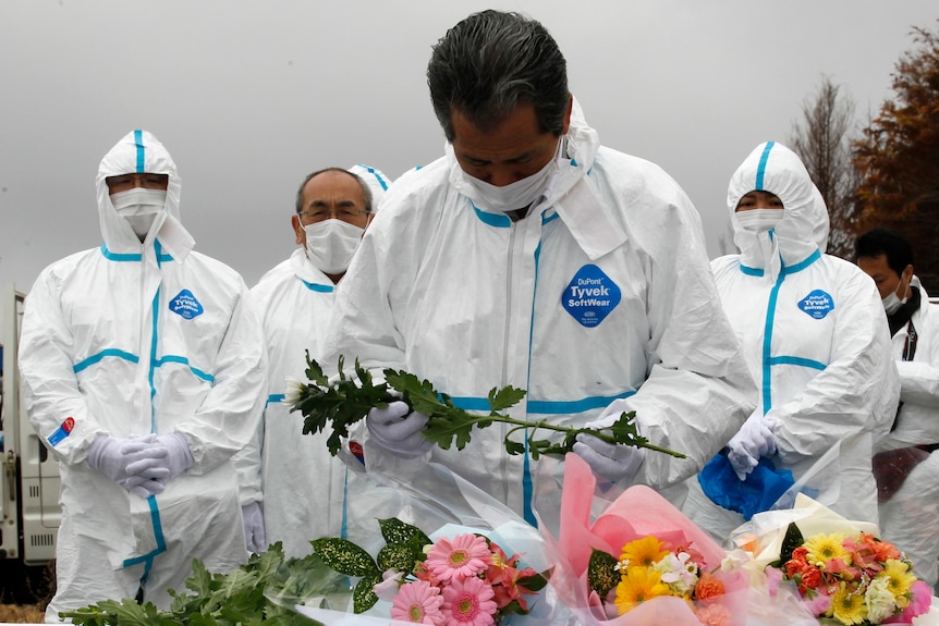 Evacuees of Okuma town, dressed in protective suits, offer flowers and prayers for victims of Japan's 2011 disaster.