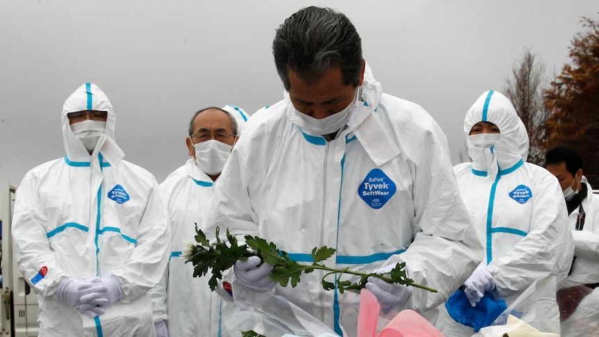 Evacuees of Okuma town, dressed in protective suits, offer flowers and prayers for victims of Japan's 2011 disaster.
