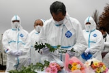 Evacuees dressed in protective suits offer flowers and prayers for victims of Japan's 2011 disaster.