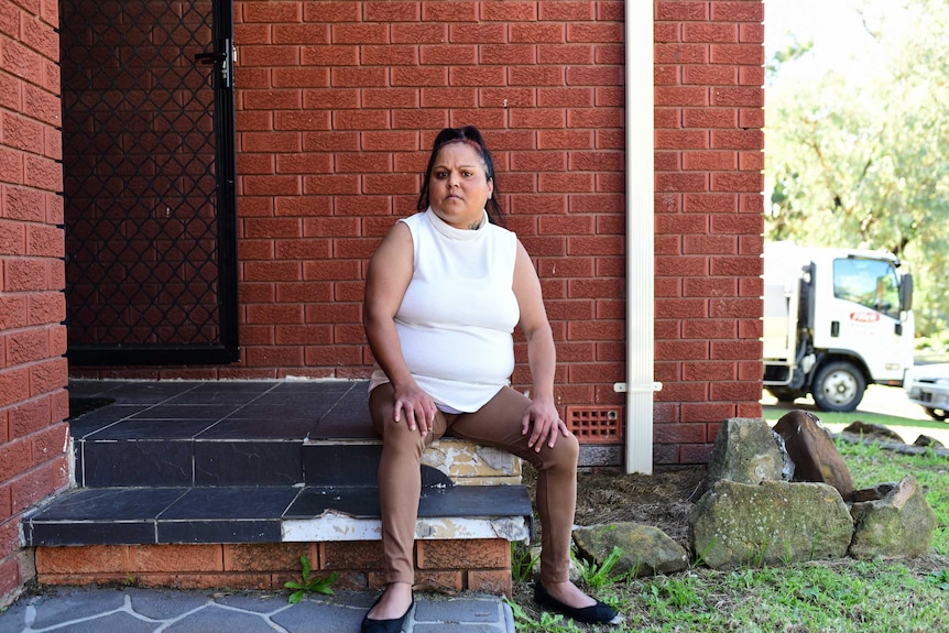Chantelle Baker sits on the steps of a red brick house.