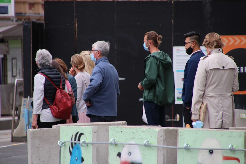 People wait at a pedestrian crossing, most wearing face masks.