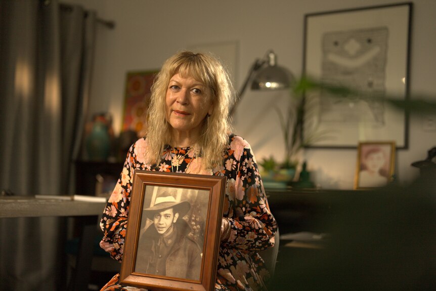 a blonde woman in a floral dress holding a photo of her father