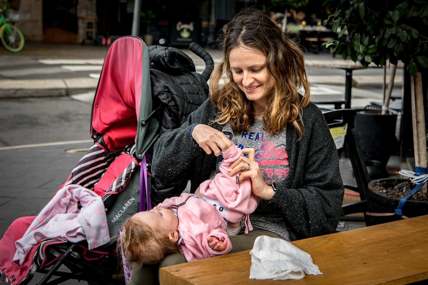 Giselle Haber changes her baby daughter Luna on a cafe table.