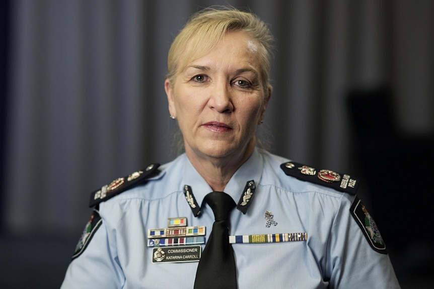 Female police commissioner in uniform with blonde hair tied up.