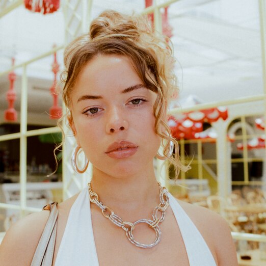 Nilüfer Yanya looks at the camera in a white halter neck top and gold jewelry