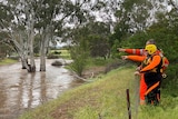 Two men wearing orange point at a creek with water in it and trees