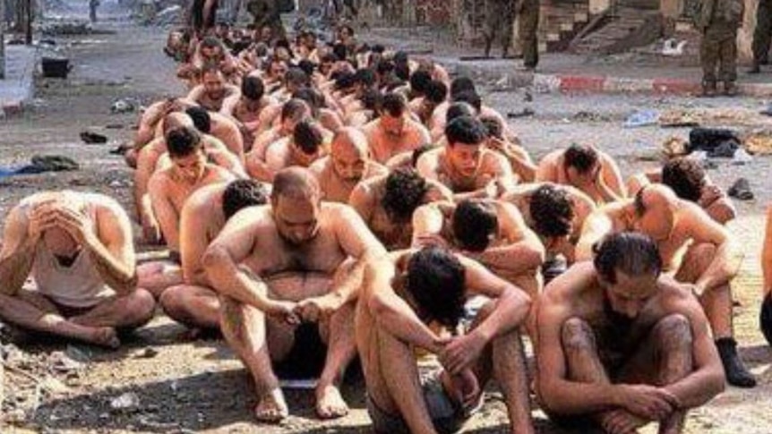 Men sitting on the ground in their underwear with their hands tied. 