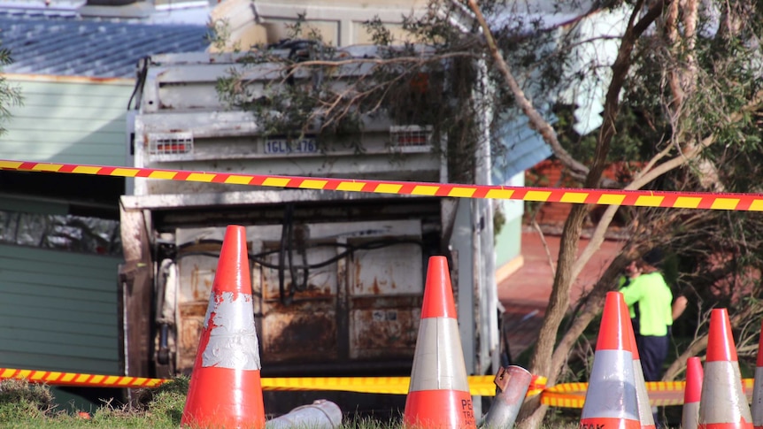 A truck is embedded in the wall of a building, with witches hats and emergency tape in the foreground.