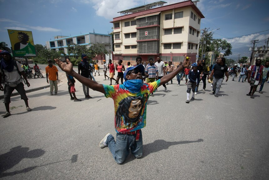 A demonstrator in a tie-dyed Bob Marley shirt prays on his knees during a protest