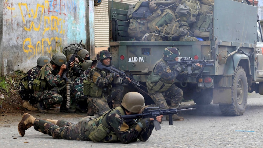 Philippines government troops crouch on the ground and prepare to fire their weapons.