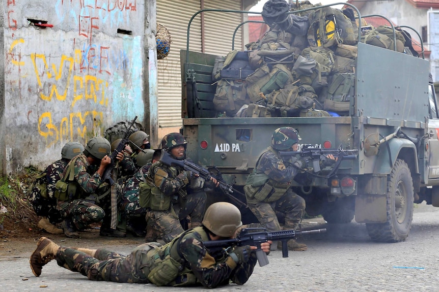 Philippines government troops crouch on the ground and prepare to fire their weapons.